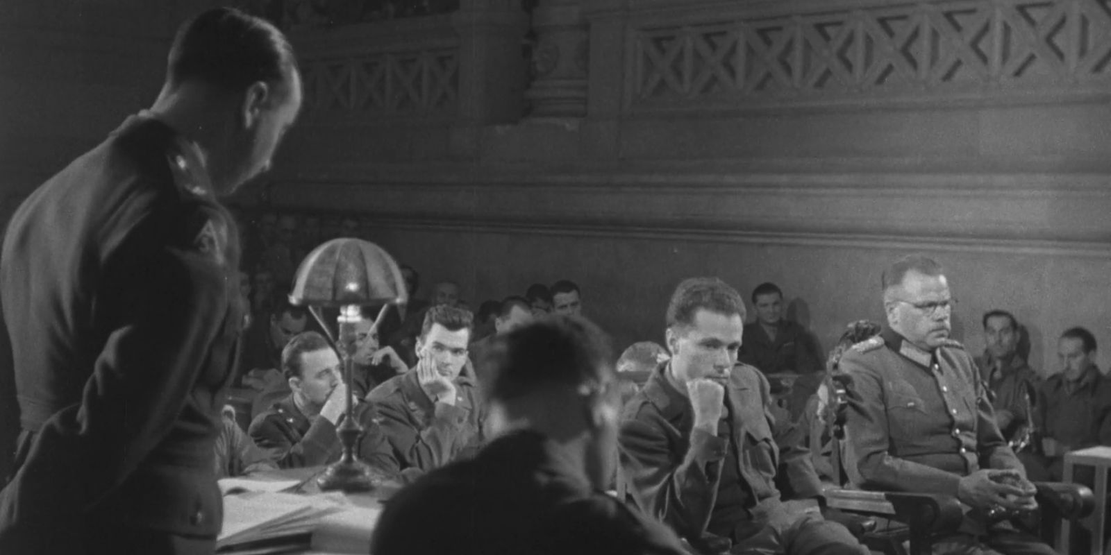 O General Anton Dostler (à direita) é retratado ao lado de seu intérprete, Albert O. Hirschman, durante seu julgamento por crimes de guerra em 1945. Este tribunal militar, realizado em Caserta, Itália, foi um marco na história jurídica, estabelecendo o precedente de que "ordens superiores" não justificam a execução de crimes de guerra. Fonte: United States Holocaust Memorial Museum.