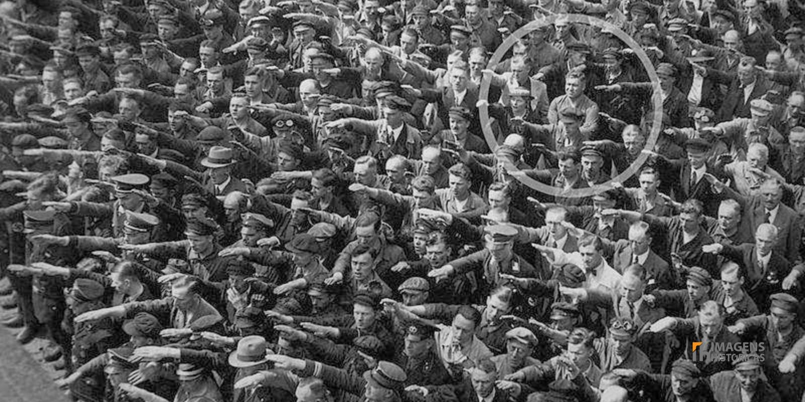 August Landmesser, de braços cruzados, em meio a uma multidão que realiza a saudação nazista durante o lançamento do navio Horst Wessel em 1936. Esta imagem icônica captura August Landmesser em um ato de desafio silencioso, recusando-se a fazer a saudação nazista em 1936. Seu gesto de coragem se destacou em meio à conformidade, tornando-o um símbolo de resistência individual contra a opressão do regime. August Landmesser, de braços cruzados, em meio a uma multidão que realiza a saudação nazista durante o lançamento do navio Horst Wessel em 1936. Esta imagem icônica captura August Landmesser em um ato de desafio silencioso, recusando-se a fazer a saudação nazista em 1936. Seu gesto de coragem se destacou em meio à conformidade, tornando-o um símbolo de resistência individual contra a opressão do regime.