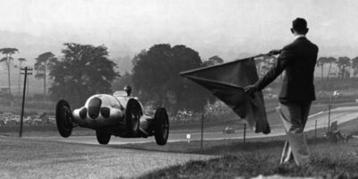 O piloto alemão Bernd Rosemeyer passa pela bandeira quadriculada a aproximadamente 130 km/h e vence o grande prêmio de Donnington Park, na Inglaterra, em 1937.