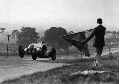 O piloto alemão Bernd Rosemeyer passa pela bandeira quadriculada a aproximadamente 130 km/h e vence o grande prêmio de Donnington Park, na Inglaterra, em 1937.