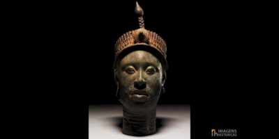 Cabeça de bronze de Ifé, criada pelo povo Yoruba na Nigéria entre os séculos XII e XIII. A escultura, feita com técnica de cera perdida, mede aproximadamente 35 centímetros e apresenta naturalismo excepcional. O rosto é coberto por linhas verticais incisas, enquanto a coroa elaborada possui múltiplas camadas de contas tubulares e borlas. Restos de tinta vermelha e preta ainda são visíveis na superfície, indicando que originalmente era policromada. Fonte: © Anthony Denselow / BBC