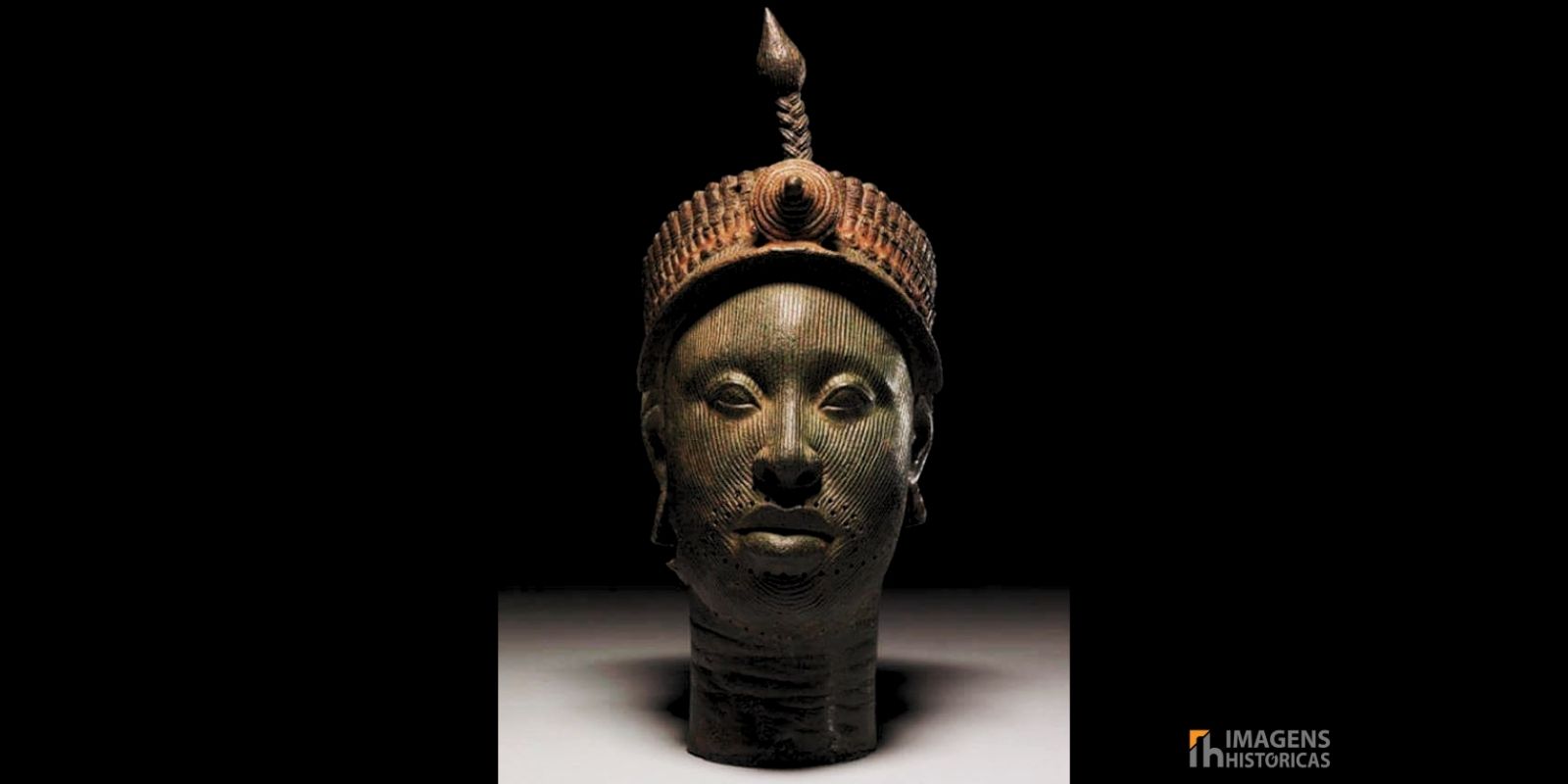 Cabeça de bronze de Ifé, criada pelo povo Yoruba na Nigéria entre os séculos XII e XIII. A escultura, feita com técnica de cera perdida, mede aproximadamente 35 centímetros e apresenta naturalismo excepcional. O rosto é coberto por linhas verticais incisas, enquanto a coroa elaborada possui múltiplas camadas de contas tubulares e borlas. Restos de tinta vermelha e preta ainda são visíveis na superfície, indicando que originalmente era policromada. Fonte: © Anthony Denselow / BBC