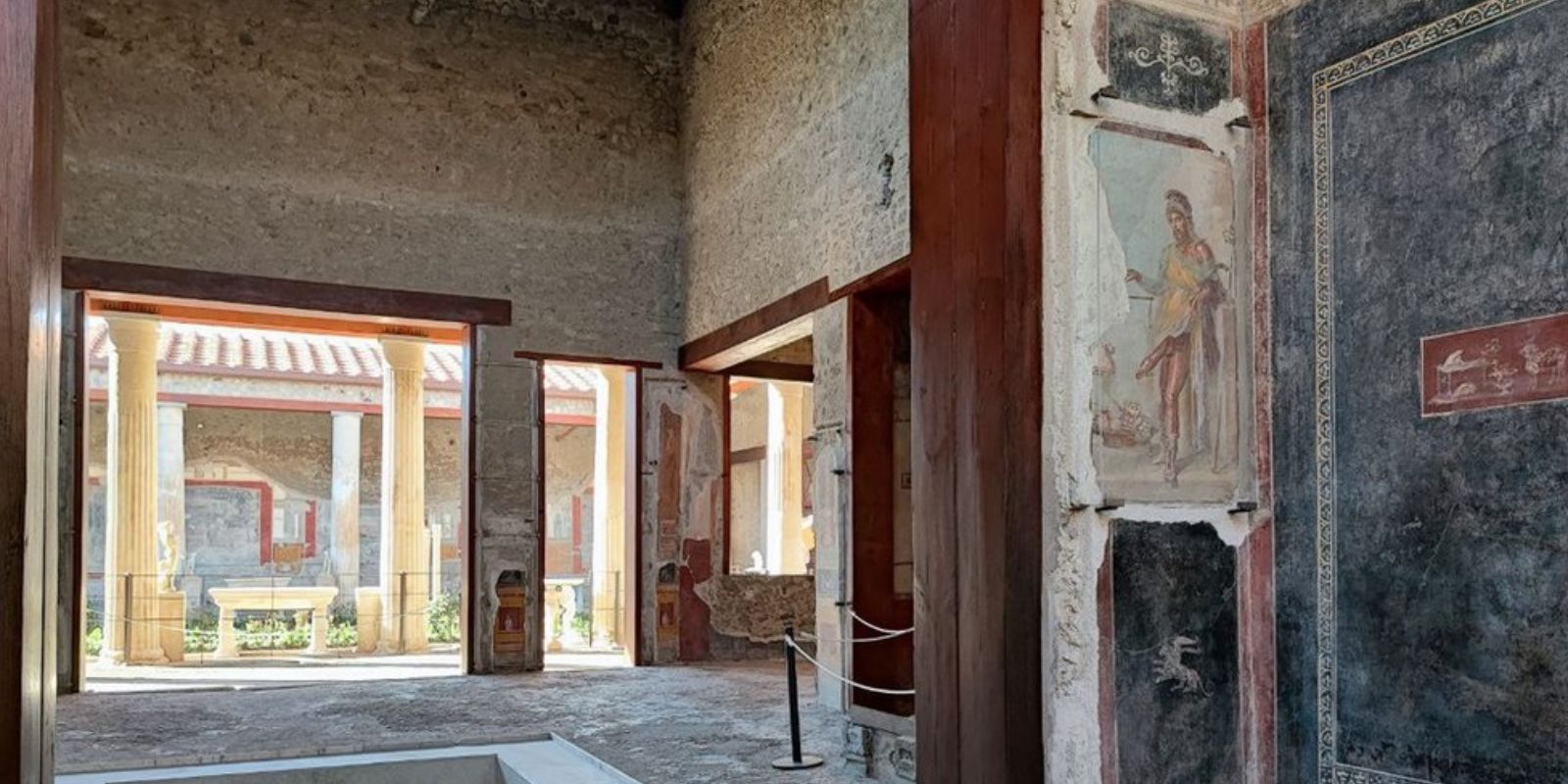 Átrio da Casa dos Vettii com vista para o peristilo, o jardim interno com colunas. Este espaço central era o coração da casa romana, onde os proprietários recebiam visitantes e clientes. A arquitetura revela o status social elevado dos irmãos Vettii.