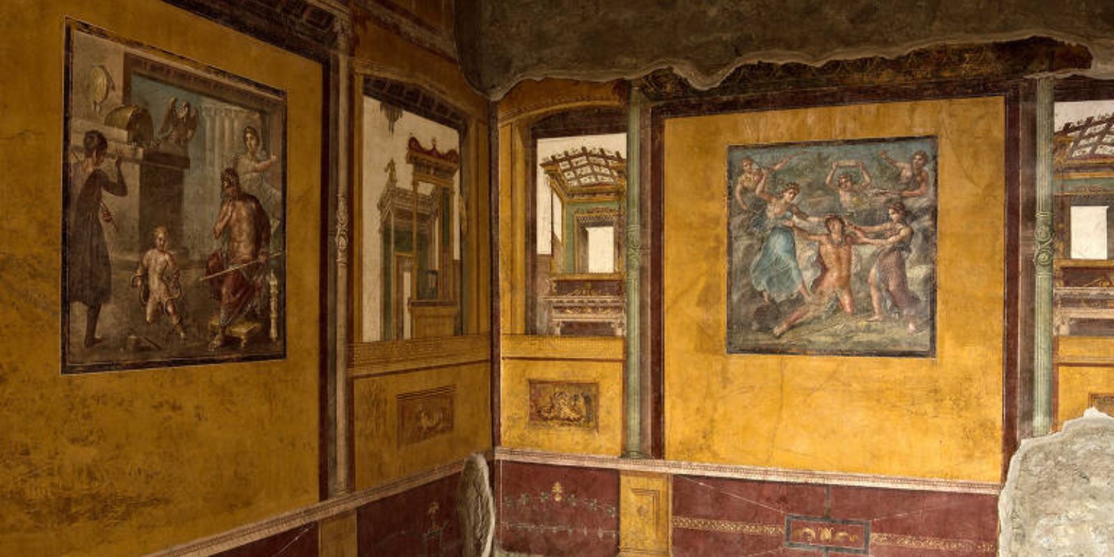 Parede com afrescos em tons de amarelo e vermelho na Casa dos Vettii. As pinturas retratam cenas mitológicas com figuras de deuses e heróis gregos. A técnica de pintura mural romana alcançou seu auge no século 1 d.C., como demonstram estas obras preservadas.