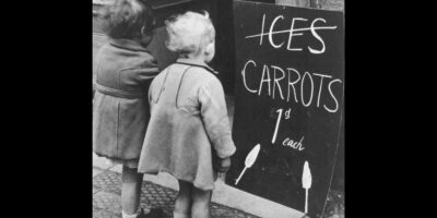 Duas crianças observam um cartaz oferecendo cenouras ao invés de sorvetes durante o grande racionamento de comida na Segunda Guerra Mundial, 1941.