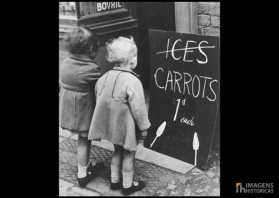 Duas crianças observam um cartaz oferecendo cenouras ao invés de sorvetes durante o grande racionamento de comida na Segunda Guerra Mundial, 1941.