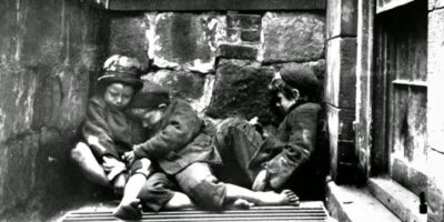 Crianças dormem nas ruas da Mulberry Street, em Nova York, por volta de 1890. Esta imagem, capturada por Jacob Riis, ilustra a dura realidade da pobreza infantil e as condições precárias de vida enfrentadas por muitas famílias imigrantes na cidade. Fonte: Jacob Riis / Museum of the City of New York.