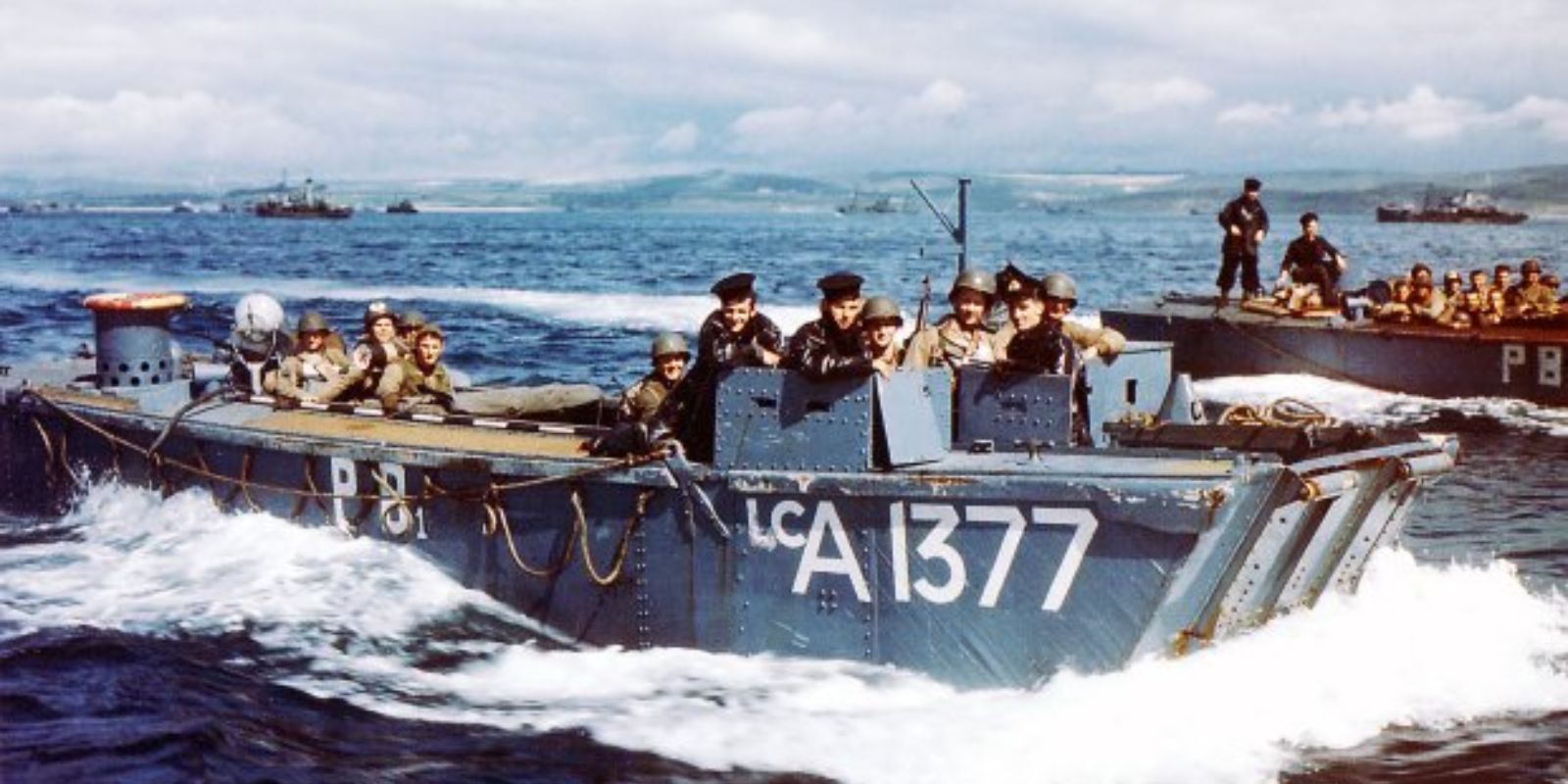 Embarcações de desembarque de assalto (LCA) britânicas, com o número de flâmula 1377, transportam tropas em direção às praias da Normandia. A imagem colorida destaca o azul do mar e o cinza das embarcações em um dia histórico. Fonte: Imperial War Museums (IWM).