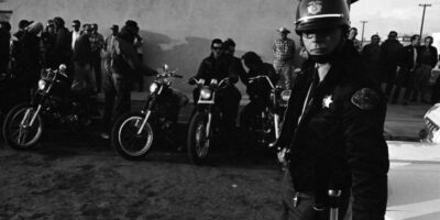 Um xerife mantém os olhos atentos do lado de fora do bar onde membros do clube de motociclistas Hells Angels utilizaram como sede do grupo durante a corrida de San Bernardino para Bakersfield em 1965.