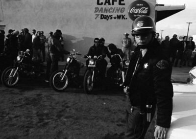 Um xerife mantém os olhos atentos do lado de fora do bar onde membros do clube de motociclistas Hells Angels utilizaram como sede do grupo durante a corrida de San Bernardino para Bakersfield em 1965.