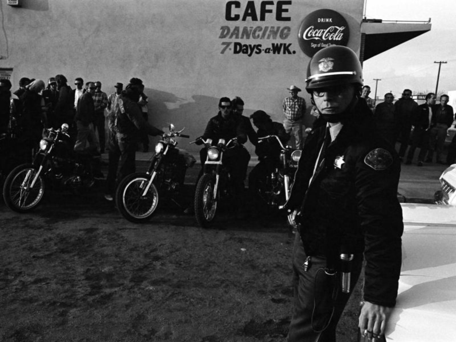 Um xerife mantém os olhos atentos do lado de fora do bar onde membros do clube de motociclistas Hells Angels utilizaram como sede do grupo durante a corrida de San Bernardino para Bakersfield em 1965. Um xerife mantém os olhos atentos do lado de fora do bar onde membros do clube de motociclistas Hells Angels utilizaram como sede do grupo durante a corrida de San Bernardino para Bakersfield em 1965.