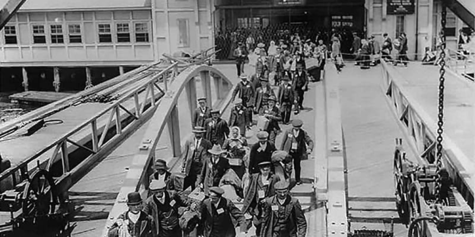 Imigrantes recém-chegados desembarcam em um porto dos Estados Unidos no início do século XX, carregando seus poucos pertences e a esperança de uma nova vida. A imagem captura o momento de transição entre a velha e a nova pátria, um rito de passagem para milhões de pessoas. Fonte: Biblioteca do Congresso dos EUA.