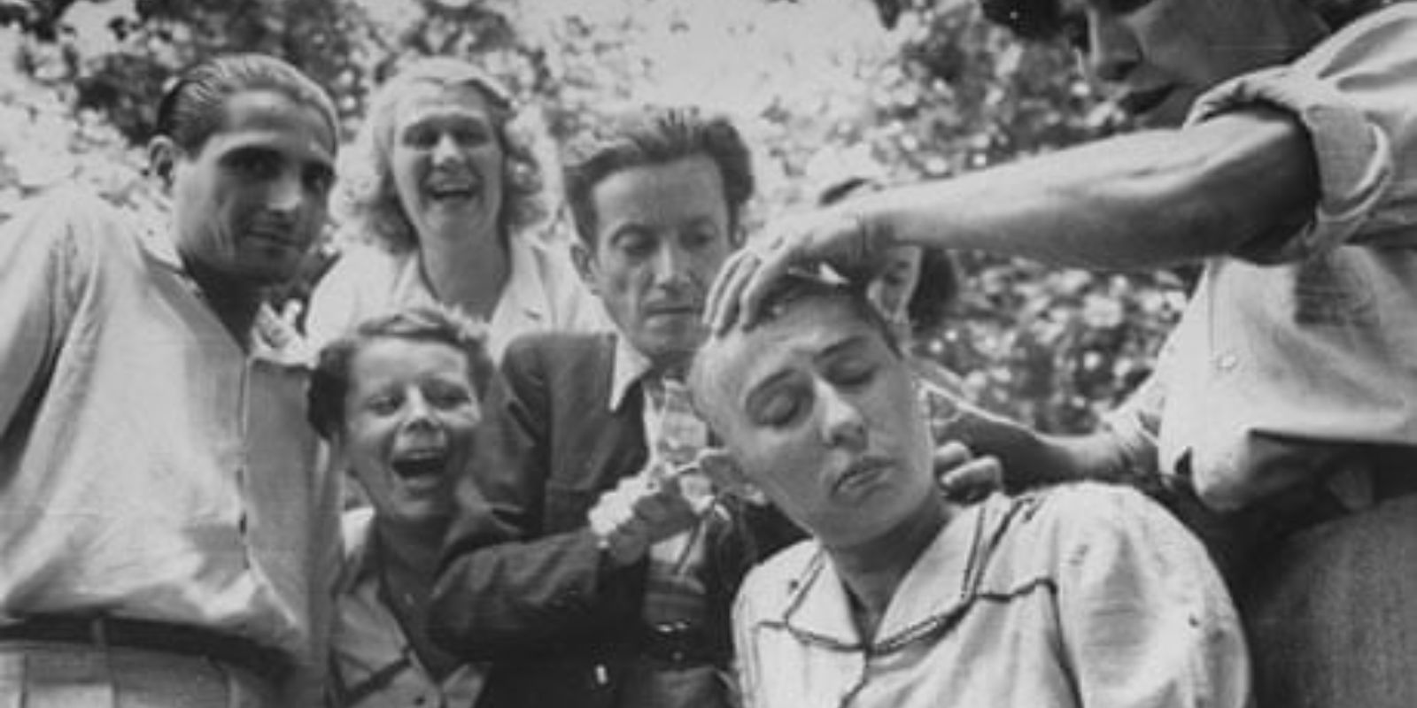 Jovens franceses zombam e apontam para uma mulher de cabeça raspada, demonstrando a crueldade e a falta de compaixão que marcaram muitos desses episódios de humilhação pública durante a libertação.