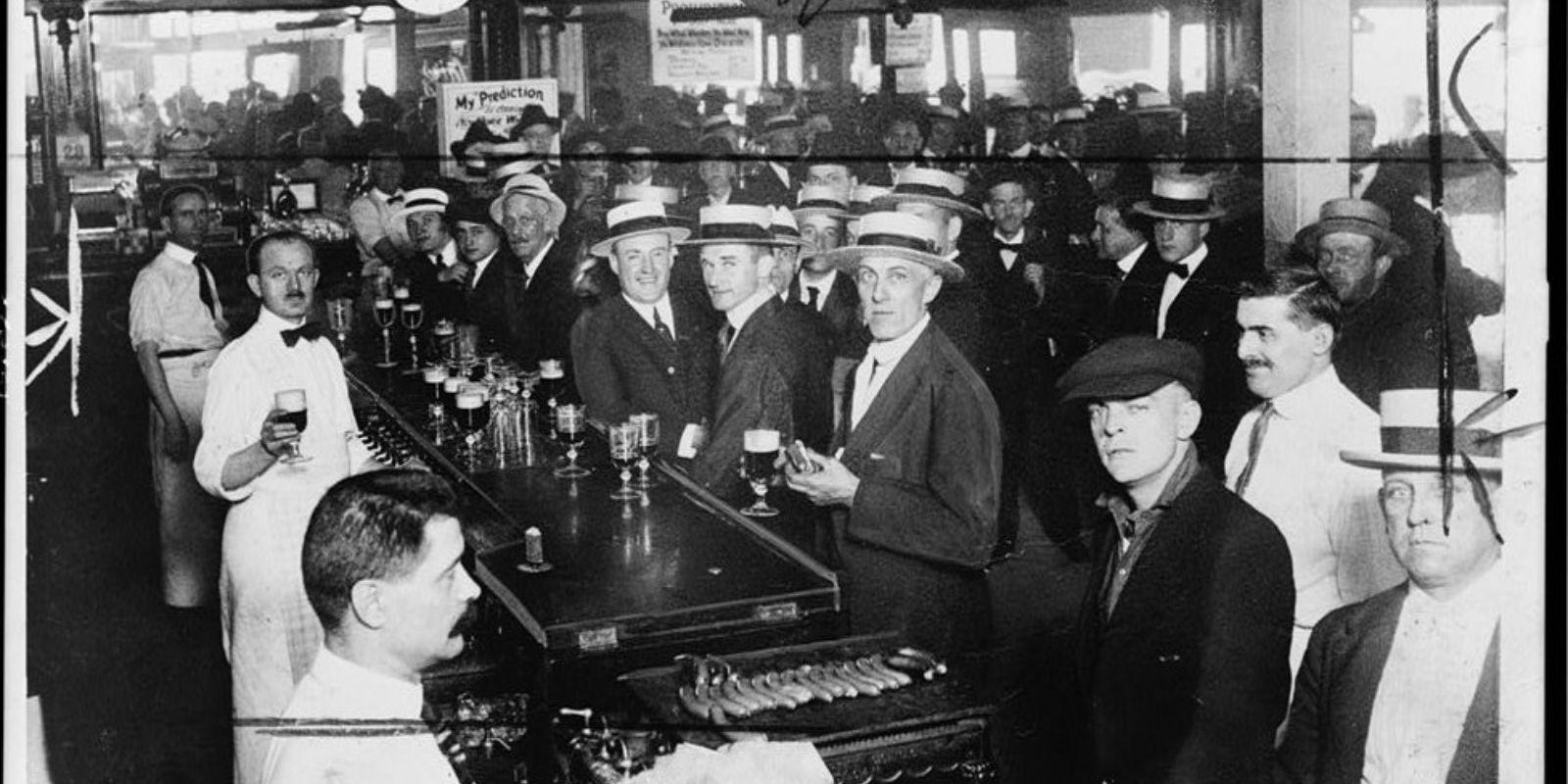 Uma visão do interior de um "speakeasy", um bar clandestino que operava secretamente durante a Lei Seca. A imagem mostra pessoas consumindo bebidas alcoólicas em um ambiente discreto, evidenciando a popularidade do comércio ilegal.