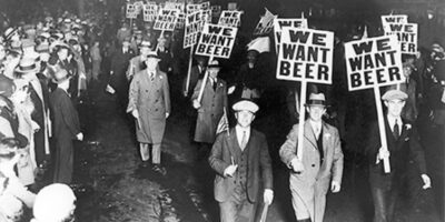 Manifestantes protestam contra a Lei Seca nos Estados Unidos, exibindo cartazes com a frase "We Want Beer" (Queremos Cerveja). A imagem reflete a insatisfação popular com a proibição do álcool e a resistência à legislação. Fonte: Library of Congress Prints and Photographs Division Washington, D.C.