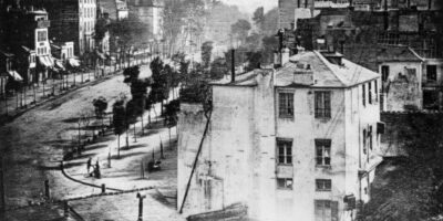 Louis Daguerre é uma figura central na história da fotografia, conhecido por desenvolver o daguerreótipo, o primeiro processo fotográfico comercialmente viável. A primeira fotografia em que aparecem pessoas (canto inferior esquerdo, na esquina), 1838. Foto: Louis Daguerre, 1838.