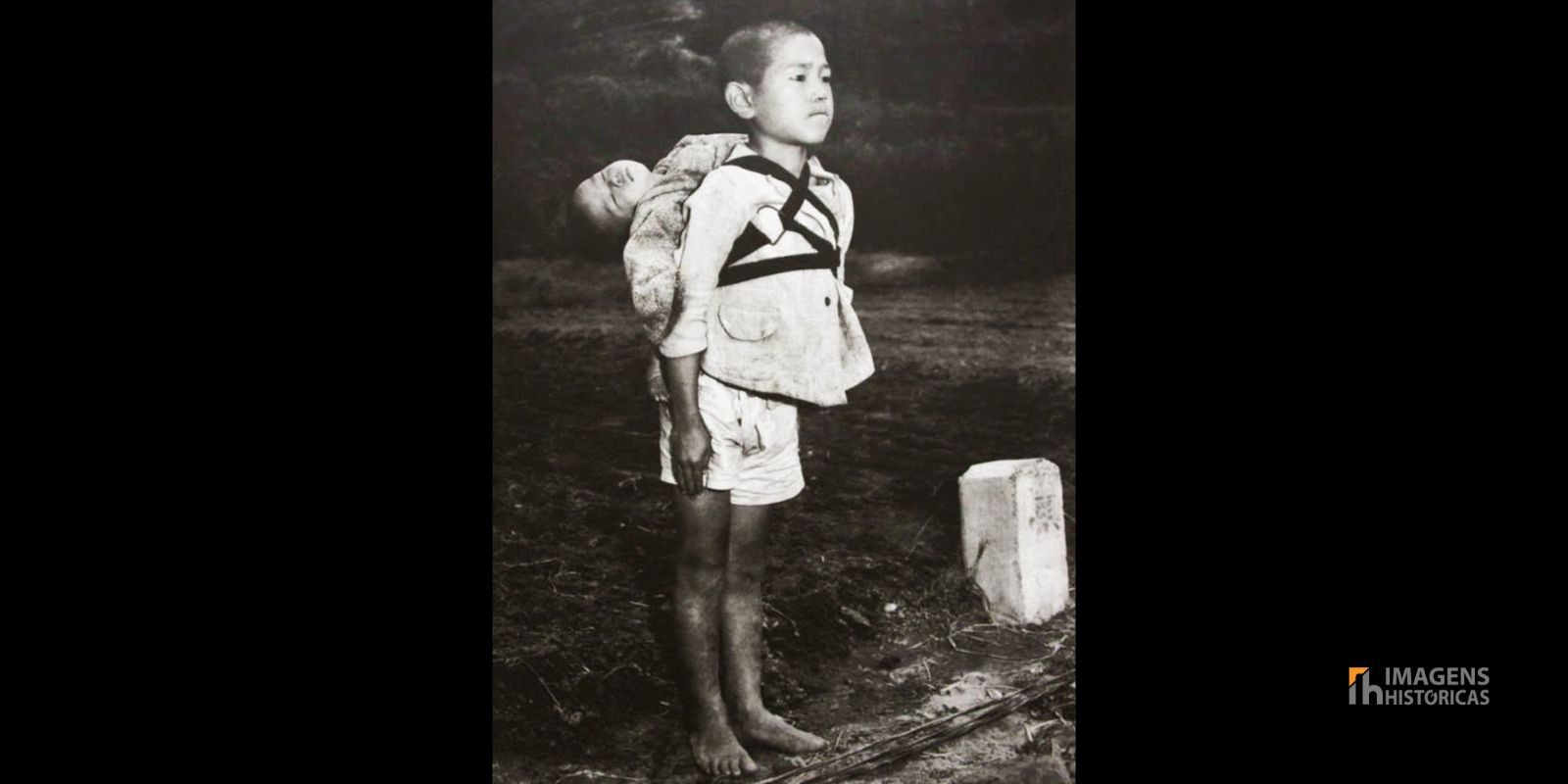 A icônica fotografia de Joe O'Donnell mostra um menino japonês em posição de sentido em frente a uma pira crematória em Nagasaki, 1945. Ele carrega seu irmão mais novo, já falecido, amarrado às costas, aguardando para entregar o corpo para a cremação. A imagem captura a dignidade e o peso do dever em meio à devastação do pós-guerra. Autor: Joe O'Donnell.