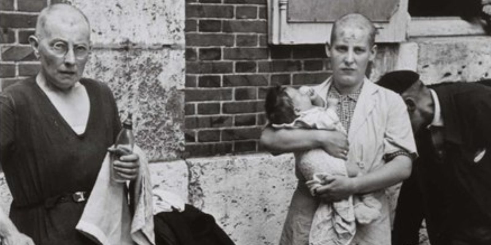 Duas mulheres francesas, com suas cabeças recém-raspadas, aguardam em pé após o ritual de humilhação pública. A expressão de resignação e dor em seus rostos revela o trauma profundo causado pela "épuration sauvage". Fonte: International Center of Photography.