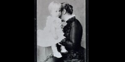 O retrato de 1882 mostra a Princesa Isabel sentada, segurando seu filho D. Antônio Gastão. Isabel veste um vestido elegante, típico da moda da época, e exibe uma expressão afetuosa e serena, enquanto o pequeno Antônio está nos braços da mãe, ainda um bebê. A composição é simples, mas eficaz, destacando o vínculo materno em um ambiente formal, típico dos retratos de estúdio da época.