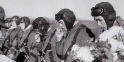 Jovens pilotos kamikazes do 72º Esquadrão Shinbu recebem flores de estudantes antes de partirem para uma missão em Okinawa, em 26 de maio de 1945. A imagem captura a mistura de cerimônia e resignação que cercava esses sacrifícios.