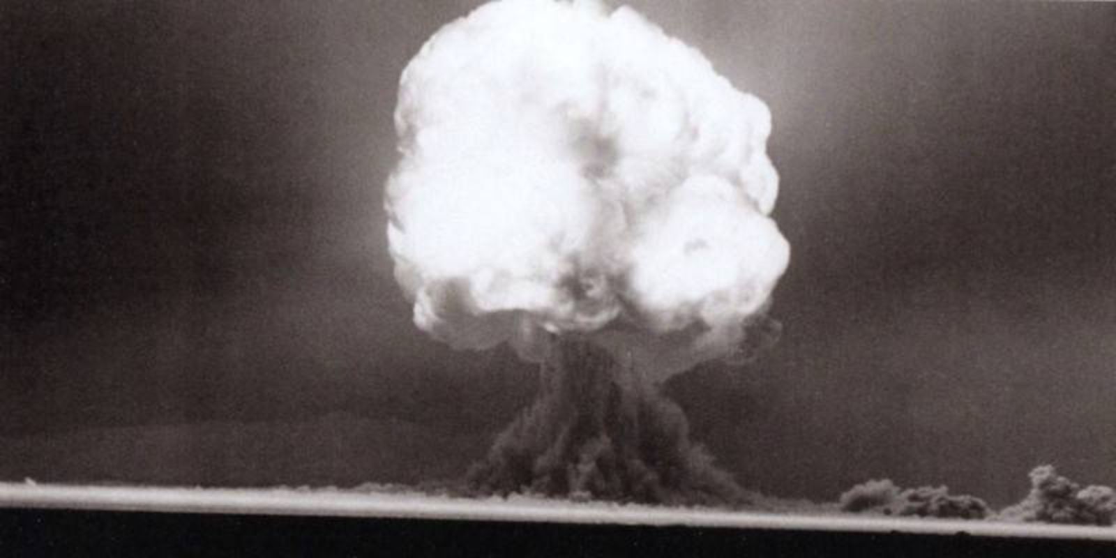 Quinze segundos após a detonação, o cogumelo atômico está totalmente formado e continua sua ascensão dramática. A estrutura clássica é agora claramente visível: uma haste (stem) escura e densa conectando o solo ao topo em expansão. O topo do cogumelo, chamado de "cap" ou cúpula, se expande horizontalmente devido à diferença de densidade com o ar circundante, criando a forma característica que se tornaria símbolo da era nuclear. Neste momento, a nuvem já atingiu entre 6 e 8 quilômetros de altitude e continua subindo rapidamente. A coloração mais escura na base indica a presença de material radioativo pesado, enquanto o topo mais claro contém principalmente vapor d'água e partículas mais leves. A nuvem eventualmente atingirá 12 quilômetros de altura, penetrando na estratosfera e espalhando material radioativo por uma vasta área. Fonte: U.S. Department of Defense.