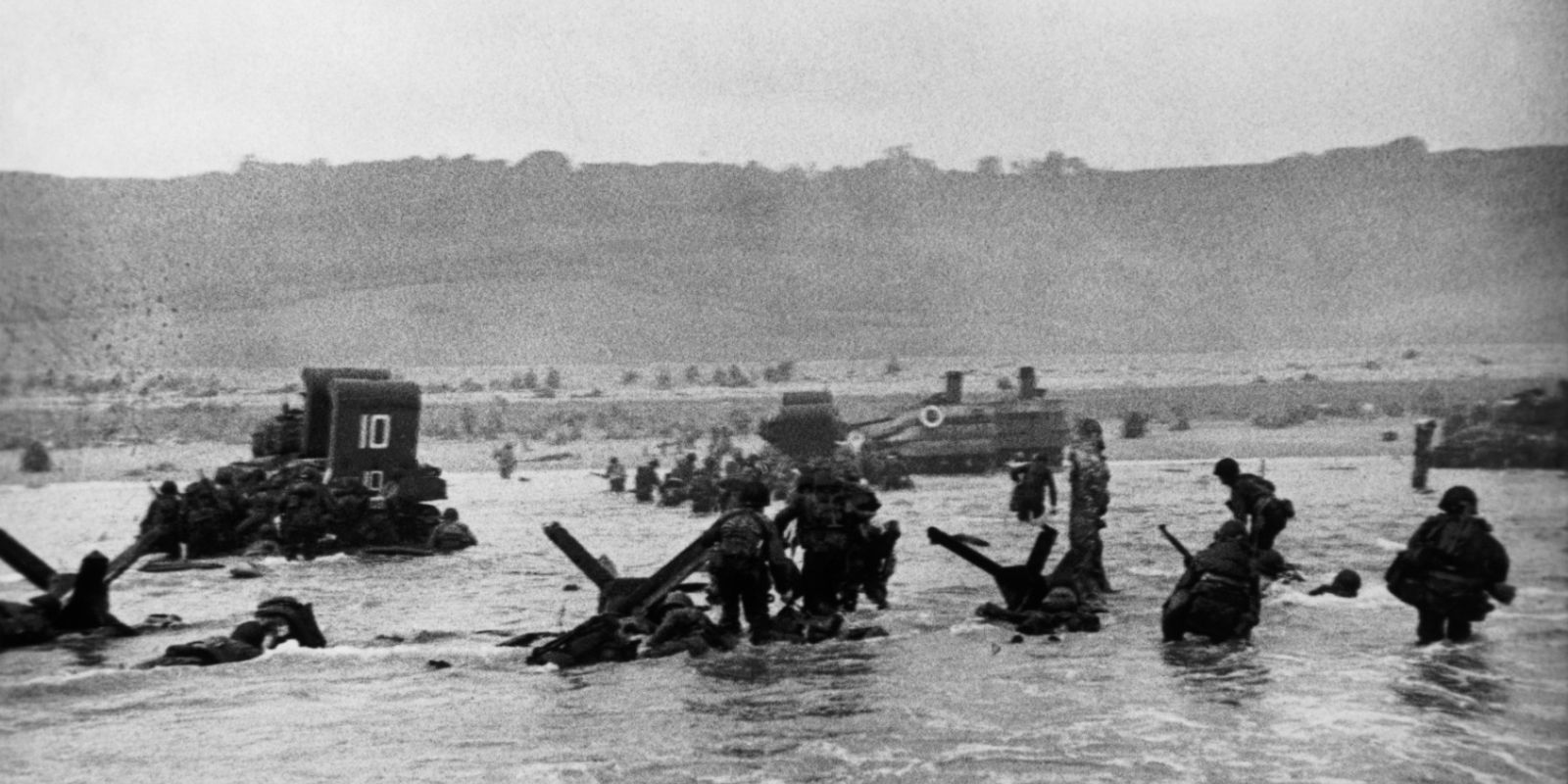 Uma das "Onze Magníficas" fotografias de Robert Capa do Dia D. Soldados americanos desembarcam na Praia de Omaha sob intenso fogo inimigo em 6 de junho de 1944. Capa foi o único fotógrafo a desembarcar com a primeira onda de tropas. A imagem tremida e ligeiramente fora de foco transmite perfeitamente o caos, o terror e a urgência daquele momento histórico. Segundo a versão oficial, apenas onze de suas fotos sobreviveram a um acidente no laboratório em Londres. Fonte: Robert Capa / Magnum Photos