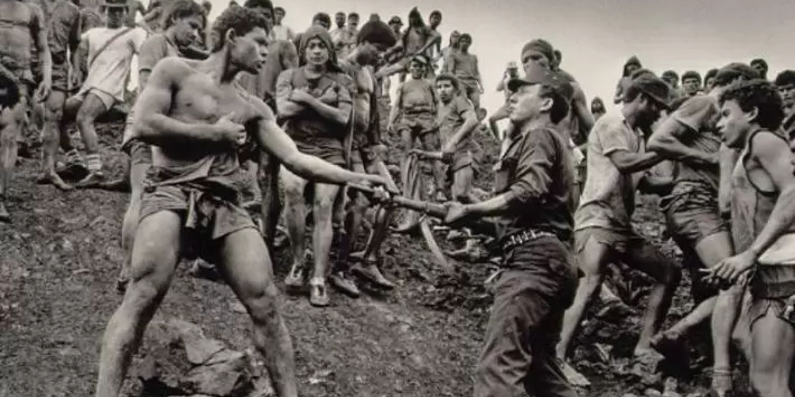 Um momento de alta tensão entre um garimpeiro e um policial militar em Serra Pelada. A imagem de Sebastião Salgado expõe a constante atmosfera de conflito e a repressão que marcaram o garimpo após a intervenção do governo federal. Autor: Sebastião Salgado.