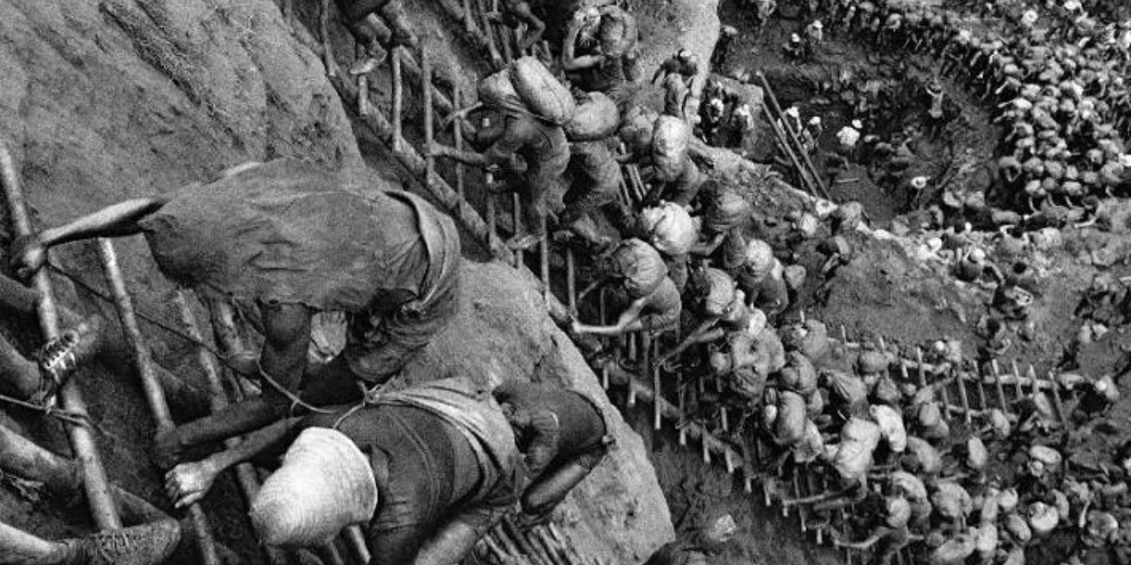 A icônica fotografia de Sebastião Salgado que imortalizou Serra Pelada como um "formigueiro humano". Milhares de garimpeiros sobem e descem as perigosas escadas de madeira, carregando sacos de terra, em uma cena que se assemelha a uma pintura épica e surreal. Autor: Sebastião Salgado.