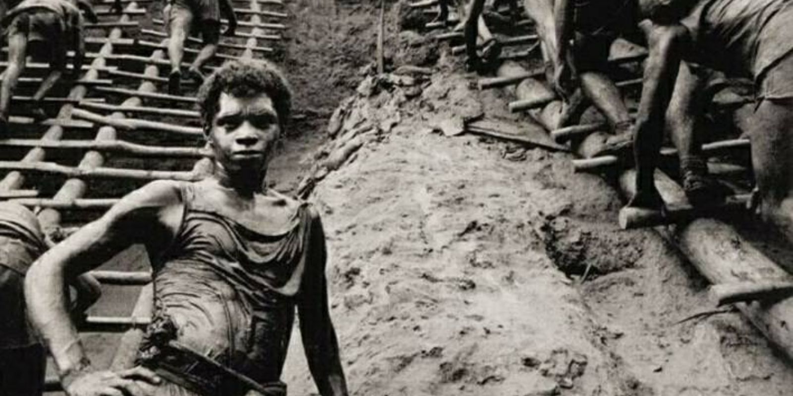 Um garimpeiro solitário, coberto de lama, encara a câmera com um olhar de exaustão e resiliência. A imagem captura a dimensão humana da tragédia e da esperança em Serra Pelada. Autor: Sebastião Salgado.