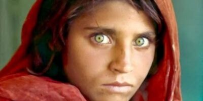 O icônico retrato de Sharbat Gula, então com 12 anos, tirado por Steve McCurry em um campo de refugiados no Paquistão em 1984. Seus olhos verdes penetrantes e sua expressão intensa a tornaram um símbolo mundial da crise dos refugiados afegãos. Autor: Steve McCurry / National Geographic.