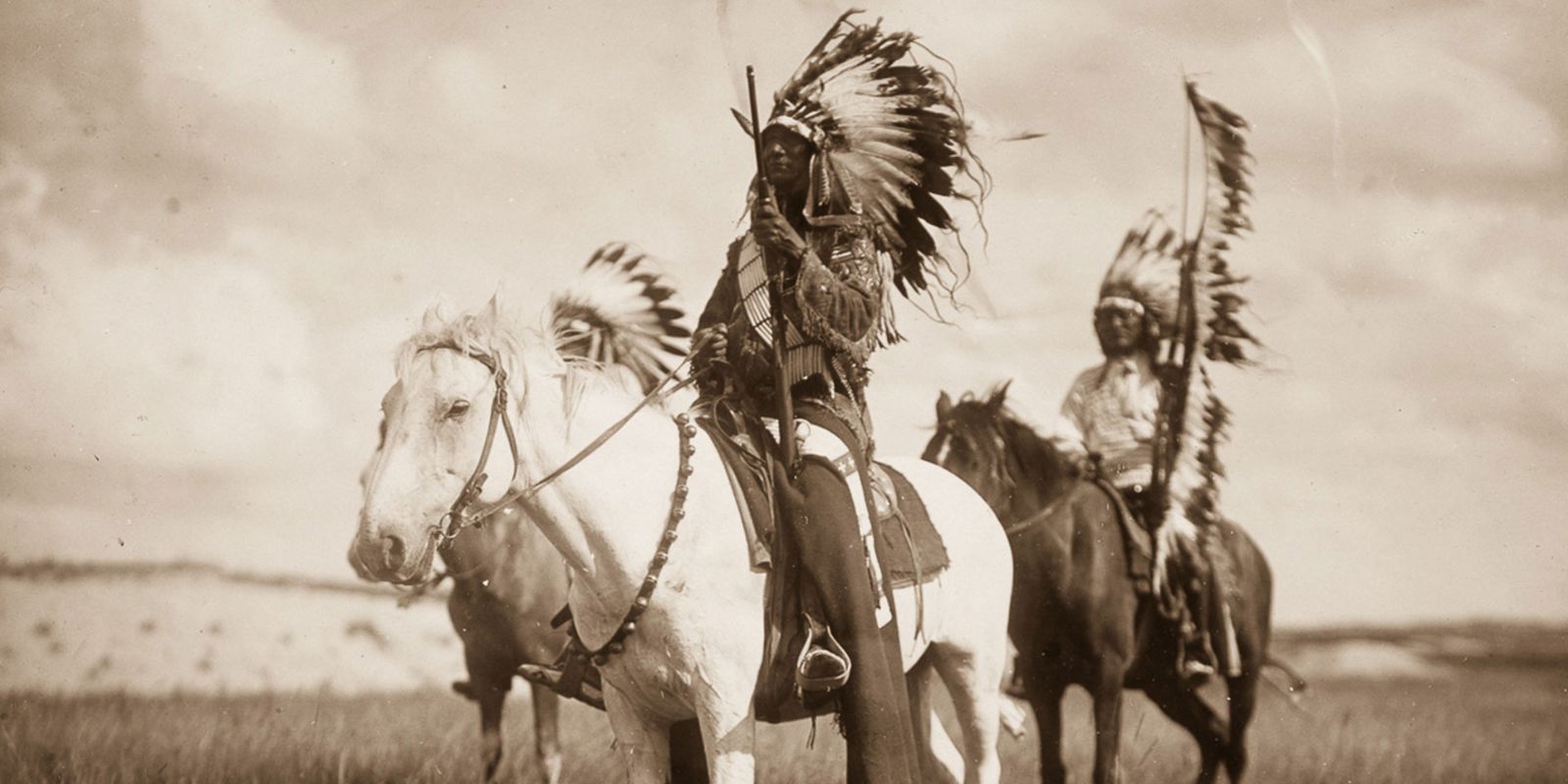 Guerreiros Sioux a cavalo nas vastas planícies, demonstrando a maestria equestre que os tornou dominantes na região. Esta imagem evoca a era de ouro da cultura das planícies, onde o cavalo era essencial para a caça ao bisão e para a defesa do território contra invasores. Fonte: Black Hills Visitor Magazine.
