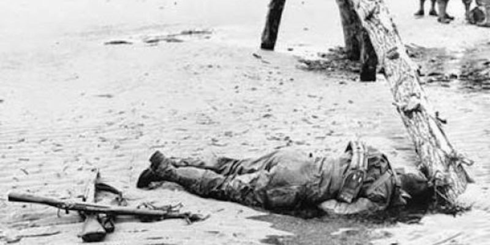Um soldado americano caído na Praia de Omaha, um lembrete sombrio do alto custo humano do Dia D. A imagem simboliza o sacrifício de milhares de soldados que deram suas vidas pela libertação da Europa. Autor: National Archives and Records Administration.