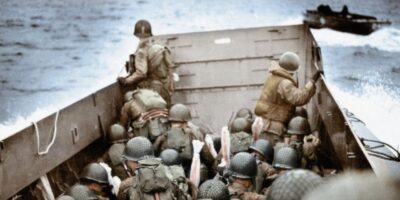 Soldados americanos se preparam para o desembarque em uma das praias da Normandia em 6 de junho de 1944. A fotografia colorida captura a tensão e a escala humana da Operação Overlord, momentos antes do confronto. Fonte: Frank Scherschel / LIFE Picture Collection.