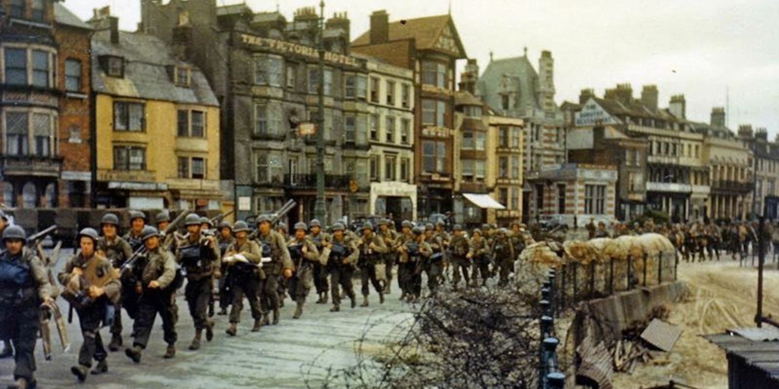 Tropas americanas marcham em formação por uma cidade costeira no sul da Inglaterra, a caminho dos navios de transporte que os levariam para a Normandia. A imagem captura a disciplina e a escala da mobilização de tropas antes da invasão. Autor: Army Signal Corps Collection / U.S. National Archives.