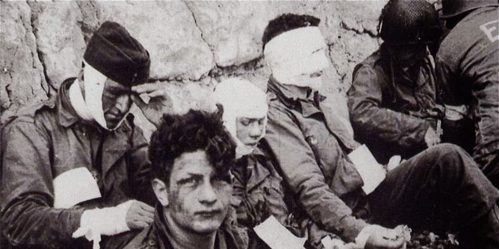 Após a sangrenta batalha, soldados feridos do 3º Batalhão do 16º Regimento de Infantaria recebem os primeiros cuidados, cigarros e comida. A imagem mostra um momento de alívio e exaustão em meio ao caos da guerra. Autor: Army Signal Corps Collection in the U.S. National Archives.