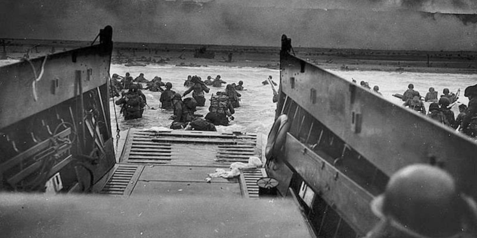 Soldados americanos desembarcam de um LCVP na Praia de Omaha, enfrentando fogo intenso de metralhadoras e artilharia alemã. A água na altura da cintura e a praia exposta tornaram o avanço extremamente perigoso, resultando em milhares de baixas. Autor: U.S. National Archives.